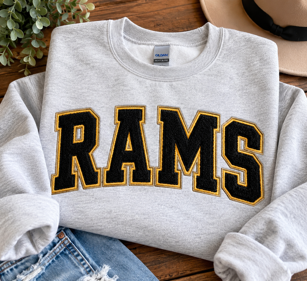 Example of a custom school spirit sweatshirt featuring black and gold RAMS lettering on a gray crewneck; actual colors and design vary by school